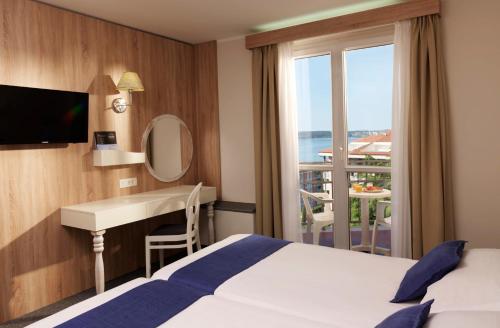 a hotel room with a bed and a desk and a window at Hotel Mirna - Terme & Wellness Lifeclass in Portorož
