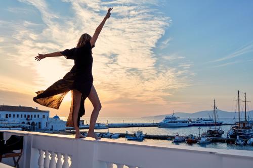a woman standing on a balcony with her arms in the air at Villa Kampani Sea View Villa Mykonos Town in Mikonos