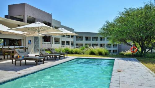 a pool with chairs and umbrellas in front of a building at Cresta Maun Hotel in Maun