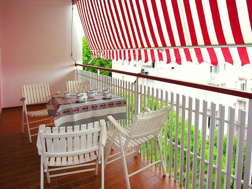 a balcony with a table and chairs and a red and white umbrella at Gabbiano Atlante in Bibione