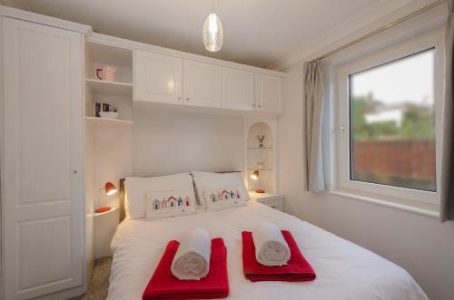 a white bedroom with two red towels on a bed at 33 The Fairway in Newton Ferrers