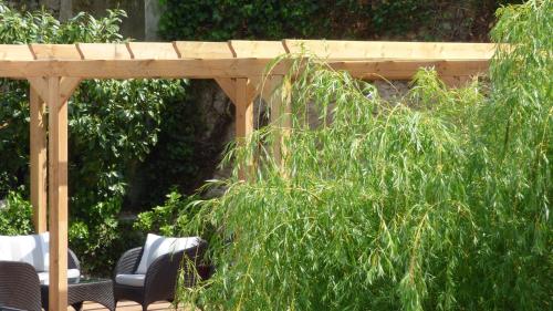 a wooden pergola in a garden with chairs and bushes at Hôtel La Tonnellerie in Beaugency