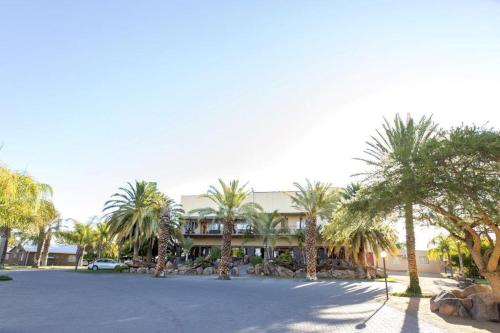 a building with palm trees in front of a parking lot at Augrabies Falls Lodge & Camp in Augrabies
