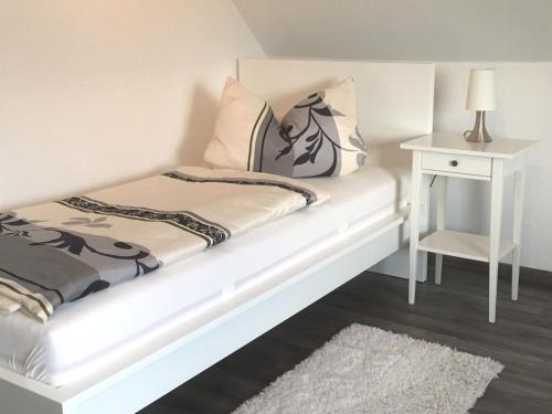 Cama blanca con mesita de noche blanca y mesa blanca en Ferienwohnung Bellevue, en Staufenberg