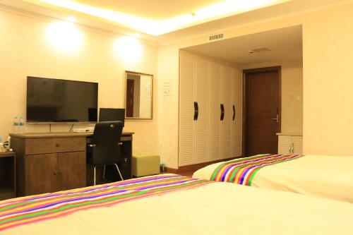 a hotel room with two beds and a desk with a television at Hanshi Hotel Yanji in Yanji