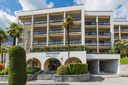 an apartment building with palm trees in front of it at Tertianum Residenza Al Parco Appartements & Restaurant in Locarno