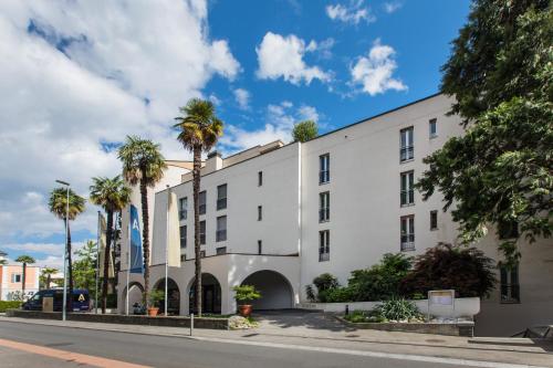 a white building with palm trees in front of it at Tertianum Residenza Al Parco Appartements & Restaurant in Locarno