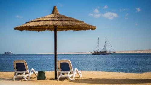 two chairs and an umbrella on a beach with a boat at Sky View Suites Hotel in Hurghada