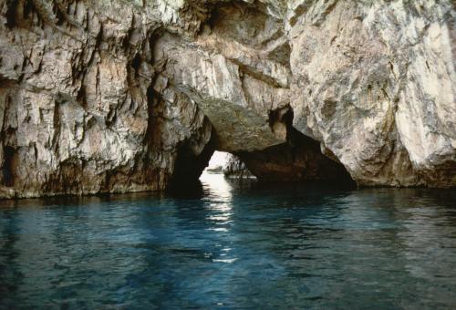 a cave in a rock wall next to the water at Apartment Stella Maris in Capri