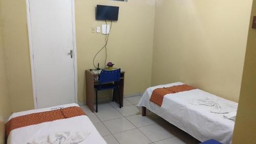 a room with two beds and a table with a desk at Hotel Brasil in Feira de Santana