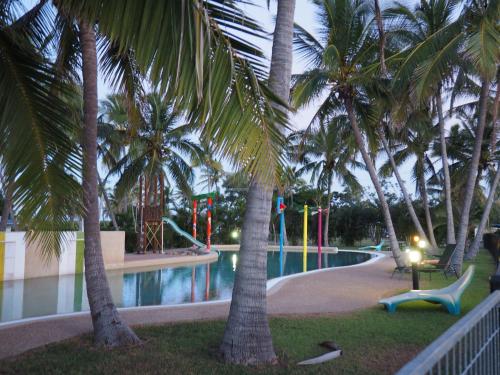 a swimming pool with palm trees in a resort at Bowen Holiday Park in Bowen