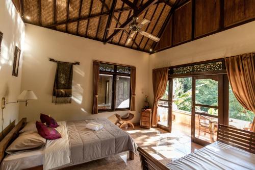 a bedroom with a bed and large windows at Bali Asli Lodge by EPS in Ubud