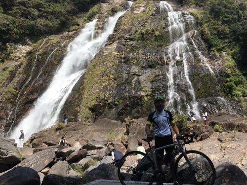 a man standing next to a bike in front of a waterfall at Yakushima Pension Luana House in Yakushima