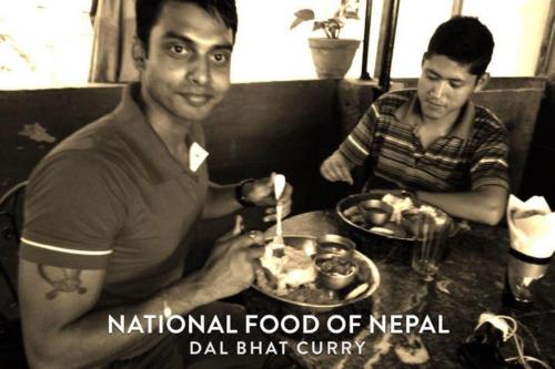 two men sitting at a table with a plate of food at Everest Home Stay Apartment in Pātan