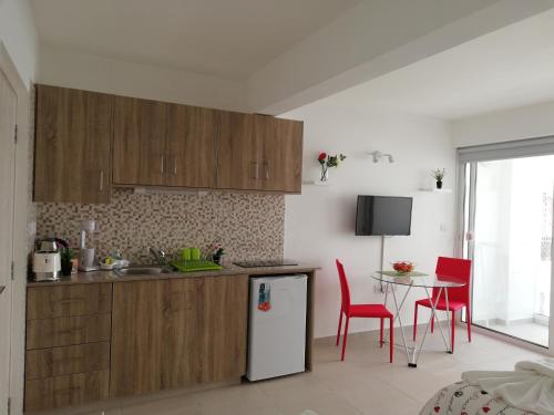 a kitchen with wooden cabinets and a table with red chairs at Chicos Studios in Ayia Napa