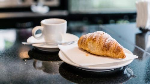 a pastry on a plate next to a cup of coffee at Flora Hotel & Suites in Merano