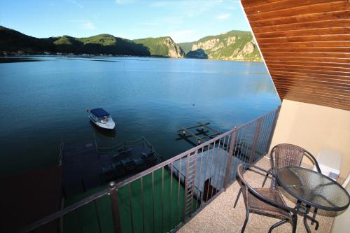 a balcony with a table and chairs and a boat in the water at Vila Golful Dunării in Dubova