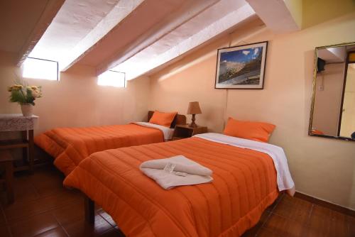 two beds in a room with orange sheets at Tambo Cusco Inn in Cusco