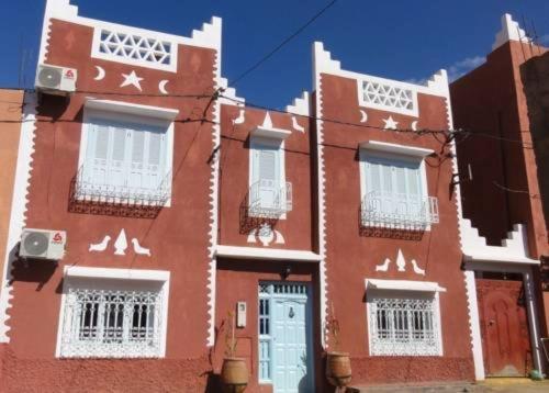 a red building with white windows and a blue door at Maison d'hôtes Dar Farhana in Ouarzazate