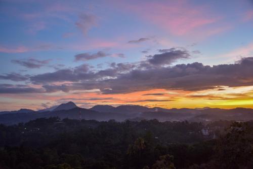a sunset in the mountains with trees in the foreground at Elegant Hotel in Kandy