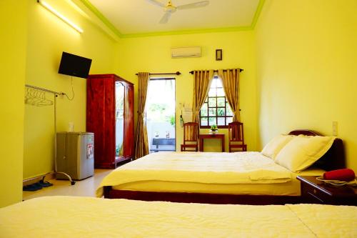 a yellow bedroom with two beds and a television at Cat Tien Guesthouse in Mui Ne