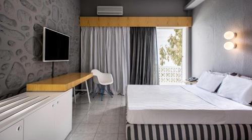 a hotel room with a bed and a desk and a tv at Alkistis Beach Hotel - Adults Only in Agios Stefanos