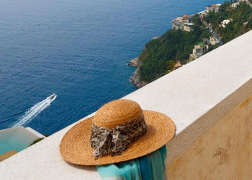 a person wearing a hat sitting on a ledge looking at the ocean at Monastero Santa Rosa Hotel & Spa in Conca dei Marini