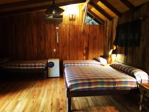 two beds in a room with wooden walls and wooden floors at Posada Camboatá in Aristóbulo del Valle