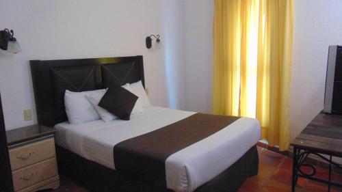 a bedroom with a bed and a television and yellow curtains at Hotel Quinta Minera in Cosalá