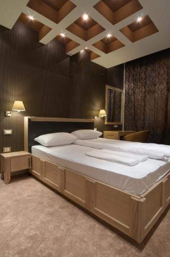 a large white bed in a room with a ceiling at Hotel Ženeva Lux in Kragujevac