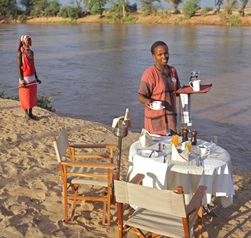 a woman standing on the beach with a table on the river at Ashnil Samburu Camp in Archers Post