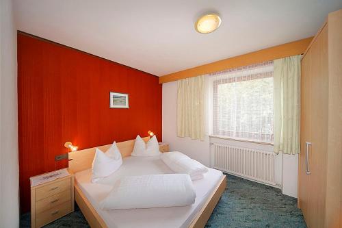 a bedroom with a white bed with an orange wall at Pension Villa Claudia Augusta in Resia