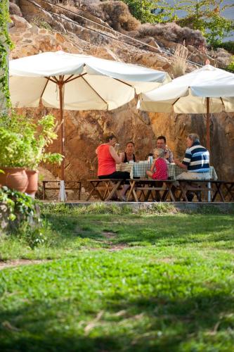 a group of people sitting at a picnic table under umbrellas at Zorbas Apartments in Volissos
