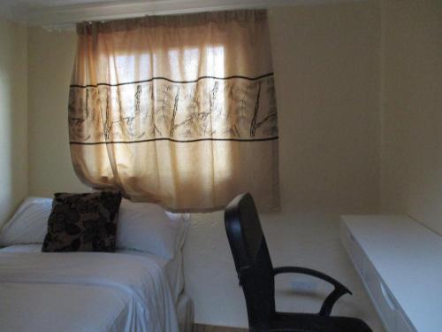 a bedroom with a bed and a chair and a curtain at Avon Apartments in Lilongwe