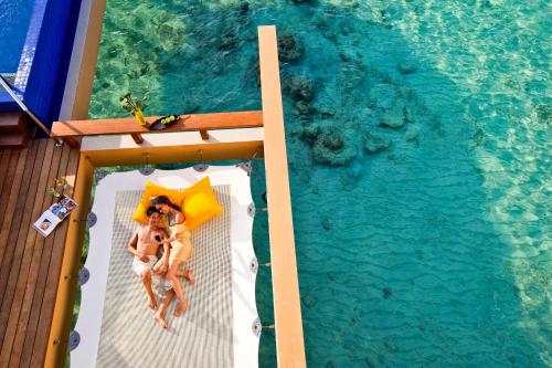 a man and a woman laying on a bed next to a swimming pool at Angsana Velavaru In-Ocean Villas - All Inclusive SELECT - Limited time offer Book 3 Nights and get 2 additional Nights Complimentary extension stay in Beachfront Villa with Half Board Meal Plan in Dhaalu Atoll