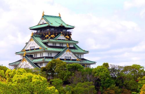 a tall building with a green roof on top of trees at Jpride Uemachidai Condo in Osaka