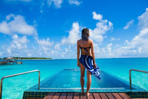 a woman in a bikini standing on a dock near the water at Angsana Velavaru In-Ocean Villas - All Inclusive SELECT - Limited time offer Book 3 Nights and get 2 additional Nights Complimentary extension stay in Beachfront Villa with Half Board Meal Plan in Dhaalu Atoll