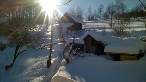 a house covered in snow with the sun shining behind it at Penzion Filoun in Plavy