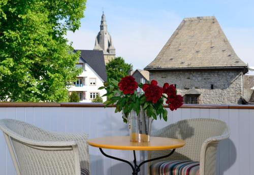 a table with a vase of red flowers on a balcony at Hotel Rech in Brilon