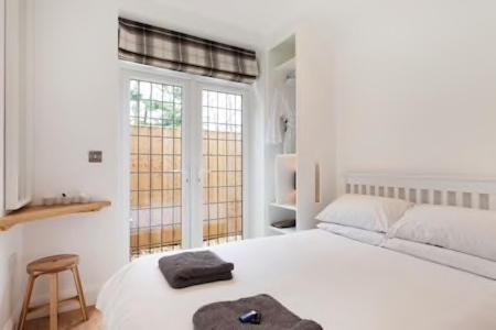 a white bedroom with a large white bed and a stool at The Woodpecker Snug in Nottingham