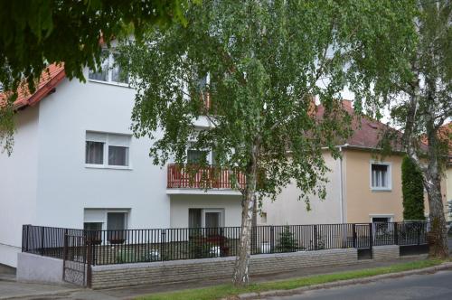 a white building with a fence and a tree at Varga Apartman Hévíz in Hévíz
