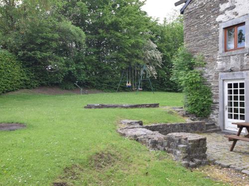 un patio con una casa de piedra con un banco y un columpio en Characteristic Arden farmhouse with Valley views, en Tenneville