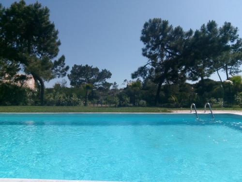 a swimming pool with blue water and trees in the background at Casa das Dunas Soltroia in Troia