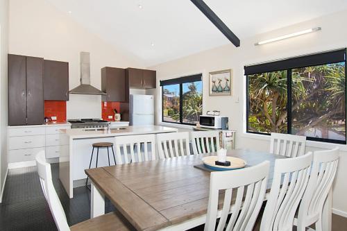 a kitchen with a wooden table and white chairs at Pandanus - Lennox Head in Lennox Head