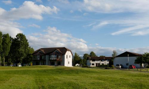 a house on a grassy field in front of a house at Macdonald Spey Valley Resort in Aviemore