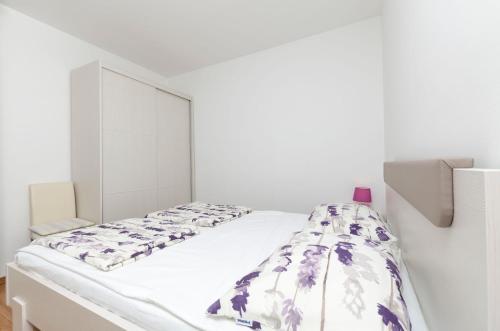 a white bedroom with a white bed with purple flowers at Apartments Danica in Primošten