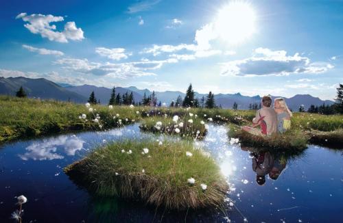 two people sitting on a patch of grass next to a pond at Schlosserhaus Appartements in Wagrain