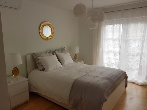 a white bedroom with a large bed and a mirror at Caia Formosa T1 in Cabanas de Tavira