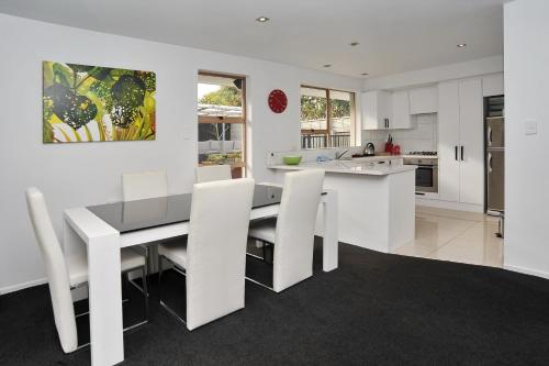 a white kitchen with a dining table and white chairs at Relaxed 3BR Hideaway - Outdoor Living & Pets - Christchurch Holiday Homes in Christchurch