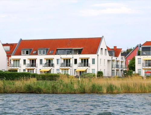 a large white building with a red roof next to the water at Ferienresidenz "Seelust" Whg 5 in Waren